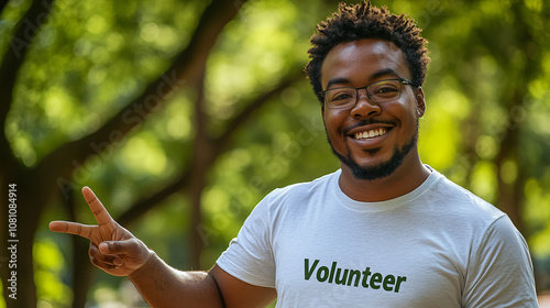 Smiling young man in a volunteer tshirt makes a peace sign gesture in a lush green park photo