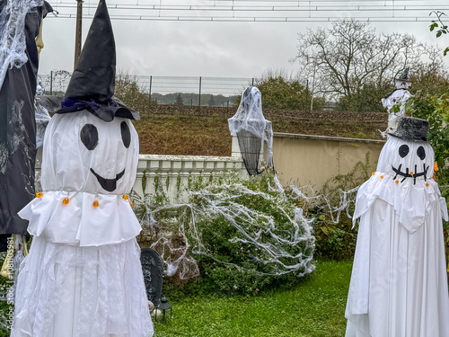 Halloween decorations featuring ghostly figures with a spooky atmosphere in a garden setting during overcast weather photo