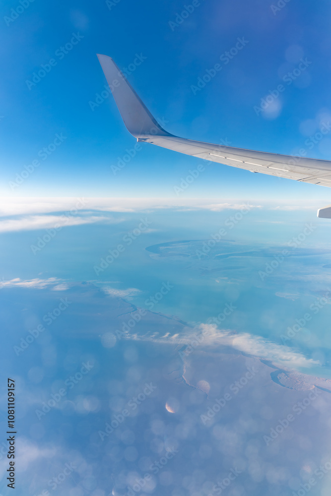 View from the airplane window at a beautiful blue clear sky, earth, sea and the airplane wing