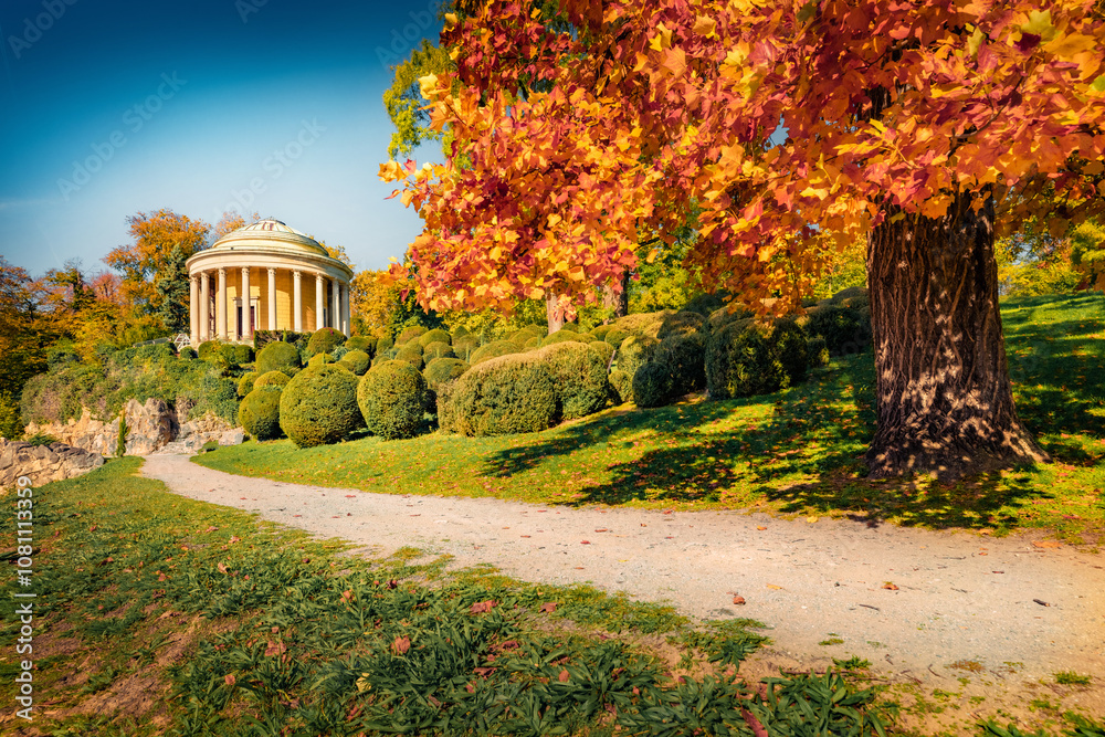 Sunny autumn view of Schlosspark Eisenstadt park with Leopoldinentempel alcove, Austria, Europe. Stunning morning of Eisenstadt, small Austrian city. Trees covered with orange and crimson leaves.