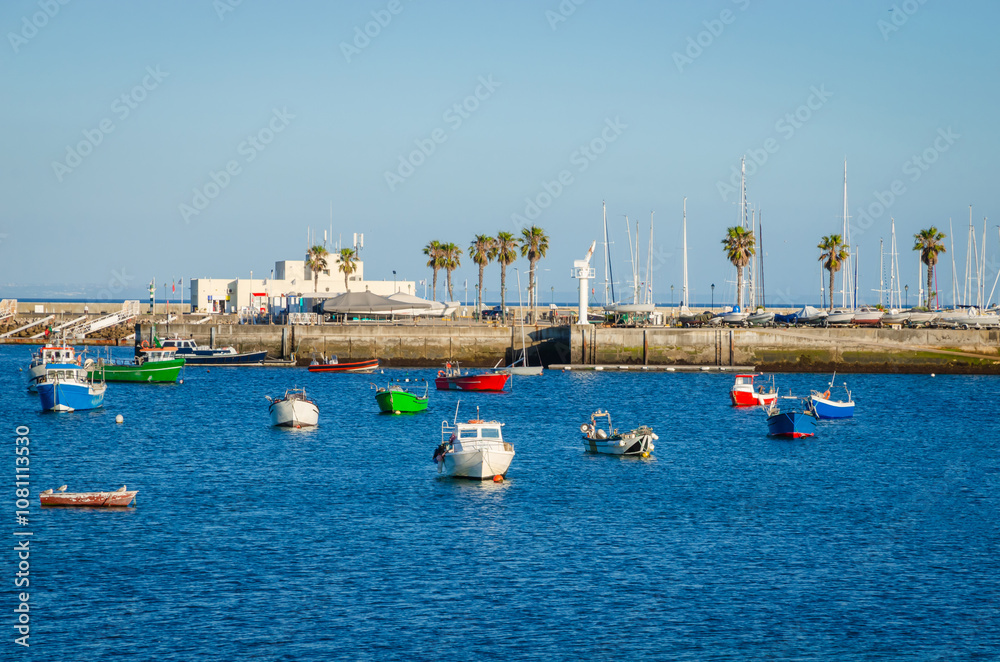 Colored fishing boats near coast of old town Cascais, Portugal, at sunset in summer day