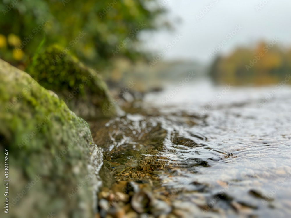 Water flowing gently over rocks by the riverbank in a tranquil natural setting during a cool morning fog Water flowing gently over rocks by the riverbank in a tranquil natural setting during a cool morning fog