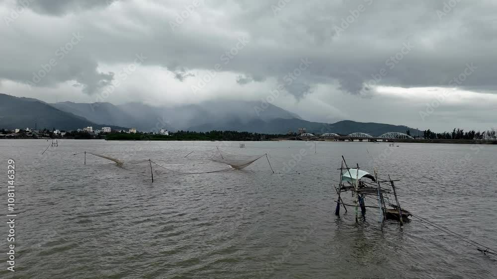Overcast sky over water with fishing nets and distant mountains, evoking serenity and monsoon themes Overcast sky over water with fishing nets and distant mountains, evoking serenity and monsoon themes