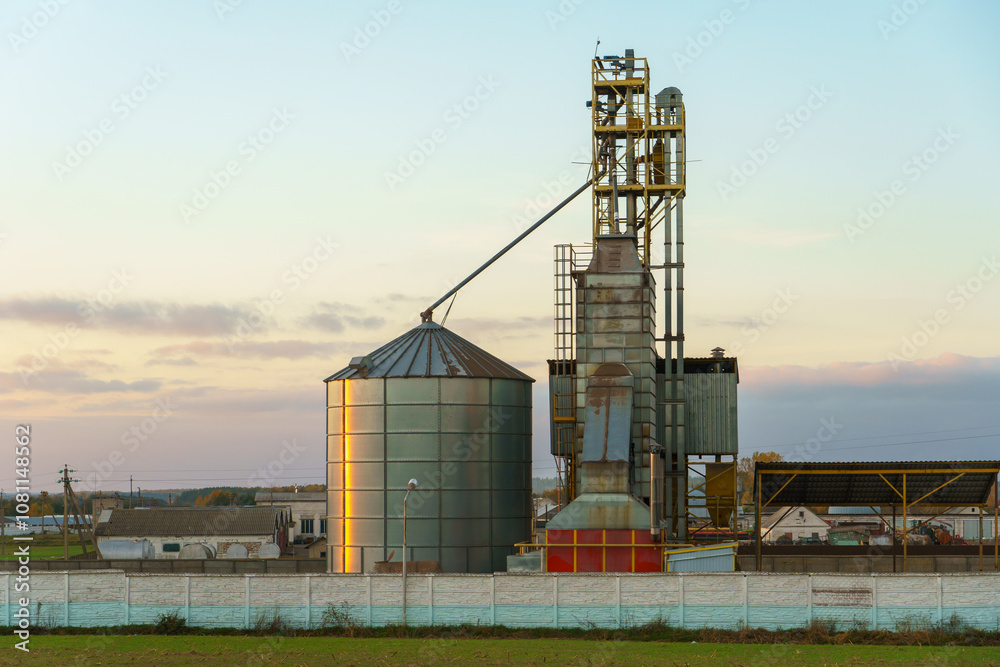 Grain silo elevator at sunset against the background of clouds. Iron barrels for grain storage. The harvest season. Grain silo elevator at sunset against the background of clouds. Iron barrels for grain storage. The harvest season.