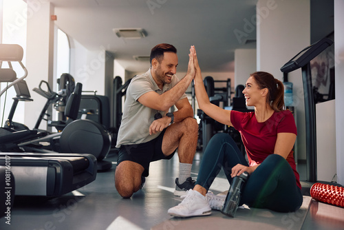Fototapeta Naklejka Na Ścianę i Meble -  Happy athletic woman and her personal trainer giving high-five after finishing sports training in gym