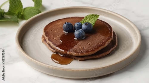 Delicious Buckwheat Pancakes with Maple Syrup: A Clean, Commercial Food Photography Highlighting Fresh Blueberries and Mint on a Light Ceramic Plate.