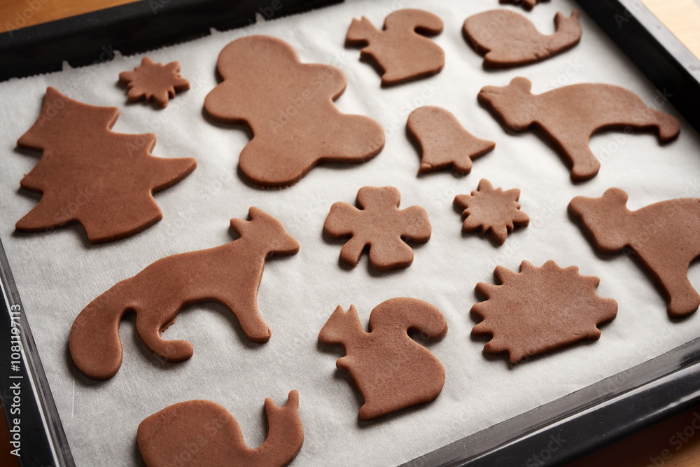 Shapes cut out from raw pastry dough on a sheet of baking paper - making gingerbread Christmas cookies Shapes cut out from raw pastry dough on a sheet of baking paper - making gingerbread Christmas cookies