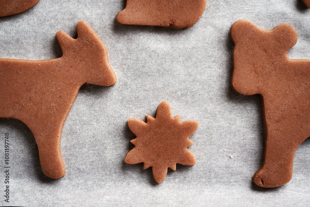 Shapes made of raw pastry dough on a sheet of baking paper - gingerbread Christmas cookies Shapes made of raw pastry dough on a sheet of baking paper - gingerbread Christmas cookies