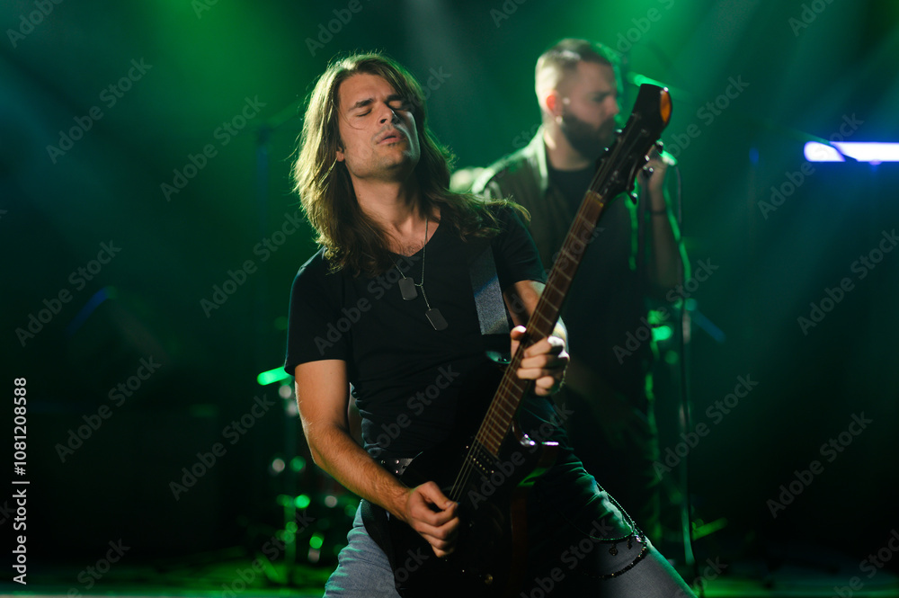 Fototapeta premium Guitarist performing live on stage with band in green lights