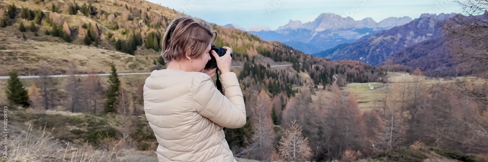 A woman in a beige jacket photographs a scenic mountain landscape in autumn, capturing nature's tranquility and beauty Dolomite Alps, Dolomites A woman in a beige jacket photographs a scenic mountain landscape in autumn, capturing nature's tranquility and beauty Dolomite Alps, Dolomites