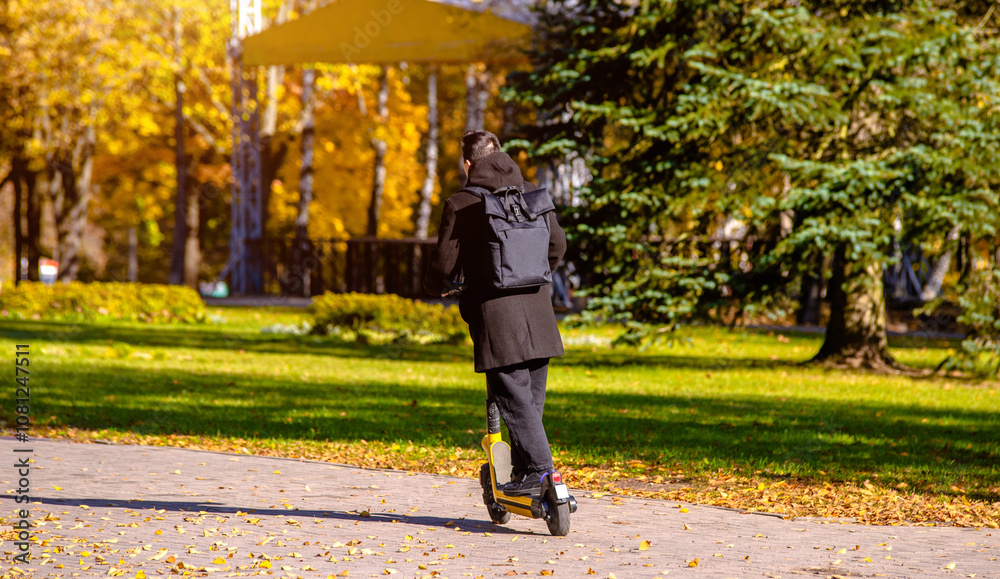 Fototapeta premium A guy rides an electric scooter in the autumn Park