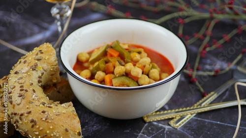 A dish of chickpeas, peppers, carrots and other vegetables with a whole grain roll