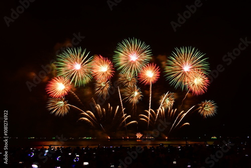 Colorful fireworks celebration with people and the city night light background at the seaside. International firework festival at Pattaya, Thailand.