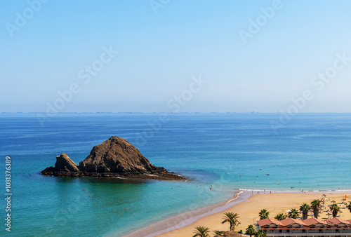 Snoopy Island in Fujairah, UAE. Aerial view of the beach with turquoise waters, a rocky island and a resort nearby