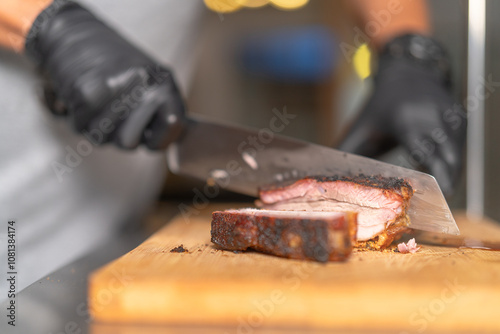 Chef slicing grilled pork belly with sharp knife on wooden board photo