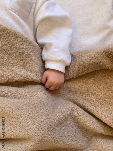 Hand of  newborn baby covered with  soft beige blanket.  Top view.  