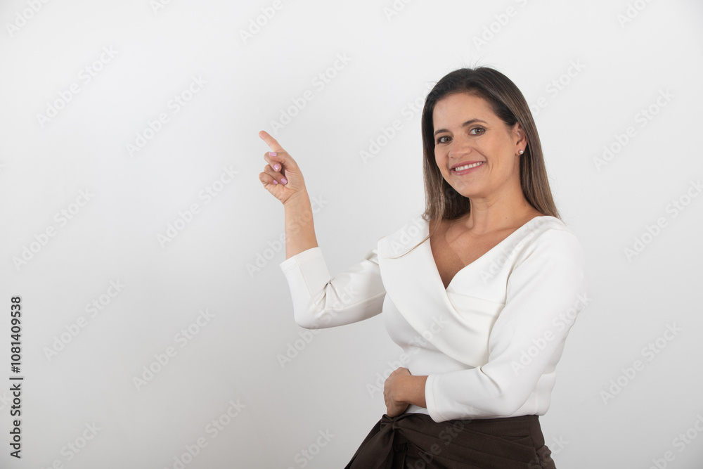 Smiling confident woman in white blouse and brown trousers pointing to the side, isolated on white background, representing guidance, presentation, leadership and modern professional style Smiling confident woman in white blouse and brown trousers pointing to the side, isolated on white background, representing guidance, presentation, leadership and modern professional style