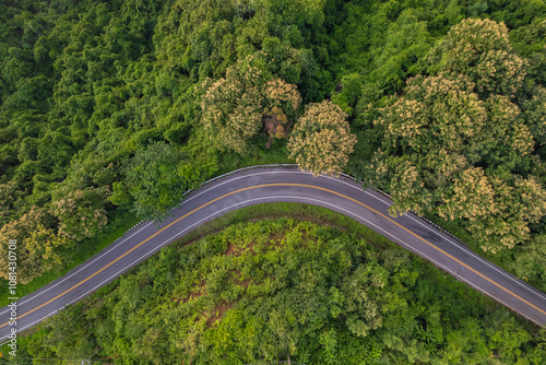 Aerial top view of countryside winding road passing through the green forest and mountain in Thailand. Ecology of system healthy environment road trip.