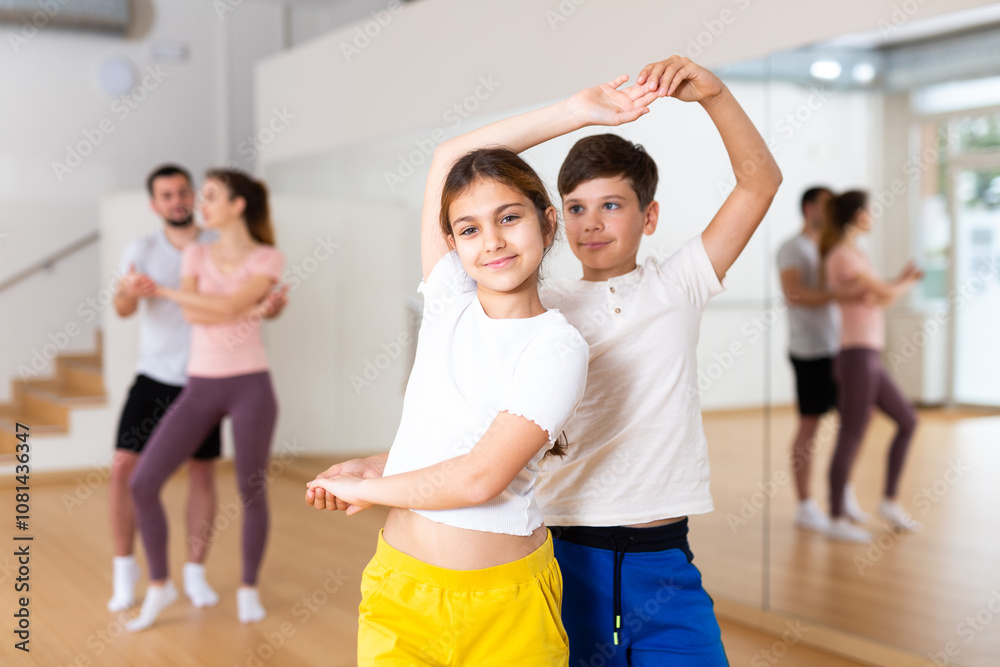 Naklejka premium Cute preteen girl and boy siblings enjoying slow foxtrot in pair in dance studio during family training with parents..