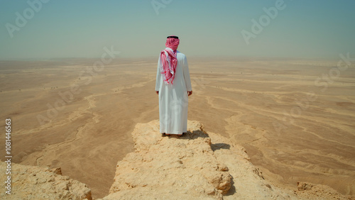 Saudi Arabian man standing on stone ledge over massive desert
