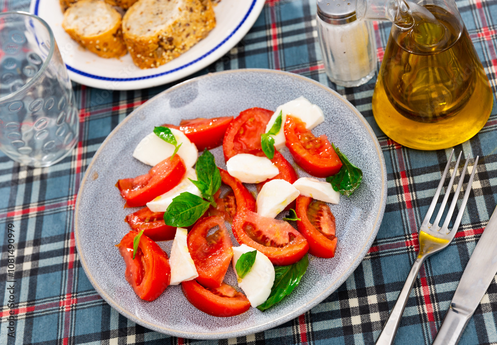 Ready-made dish of Italian cuisine is caprese salad made from slices of mozzarella cheese, slices of ripe tomatoes and basil leaves. Simple and hearty snack, independent dish Ready-made dish of Italian cuisine is caprese salad made from slices of mozzarella cheese, slices of ripe tomatoes and basil leaves. Simple and hearty snack, independent dish