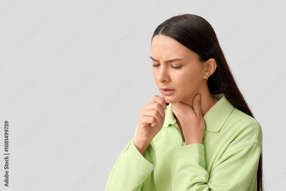 Beautiful young woman suffering from sore throat on grey background Beautiful young woman suffering from sore throat on grey background