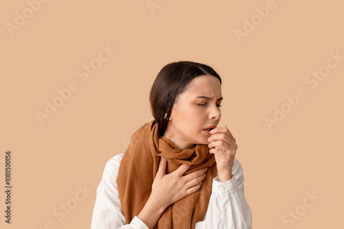 Beautiful young woman in scarf suffering from sore throat on brown background