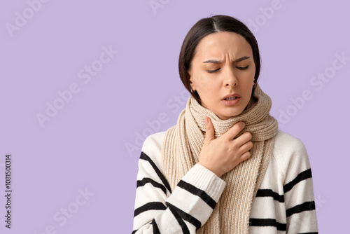 Beautiful young woman in scarf suffering from sore throat on lilac background photo