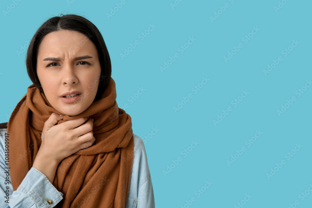 Beautiful young woman in scarf suffering from sore throat on blue background