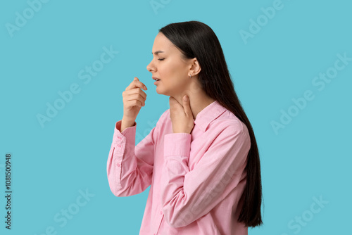 Beautiful young woman suffering from sore throat on blue background