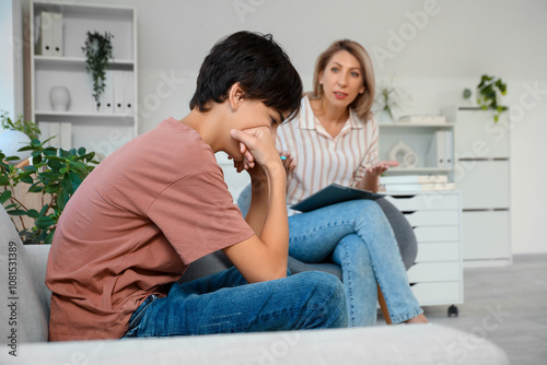 Upset teenage boy sitting on sofa at psychologist's office