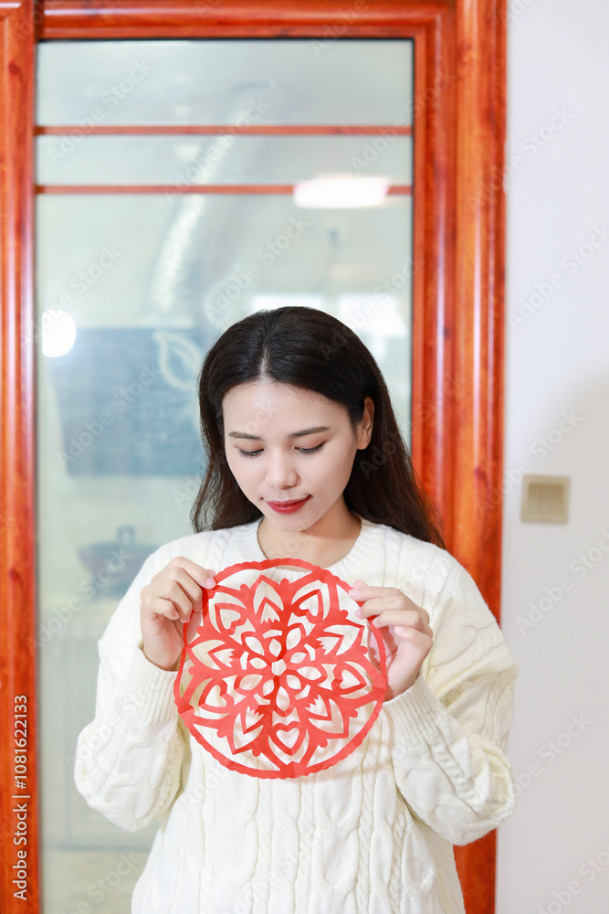 A Chinese woman putting up window decorations at home on the theme of Spring Festival A Chinese woman putting up window decorations at home on the theme of Spring Festival