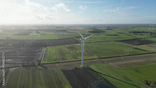 Aerial drone shot of wind turbine as the drone camera moves toward it from a higher altitude, showcasing the expansive landscape and waterlogged field surrounding the turbine. photo