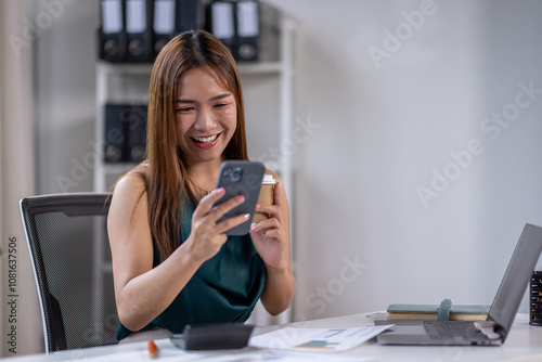 Business Asian woman hold phone and use laptop at the workplace. Project stats financial data sales charts on laptop and cellphone Asian finance concept 