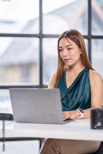 Portrait of young beautiful business asian woman sitting in front of laptop at her desk in workplace office.