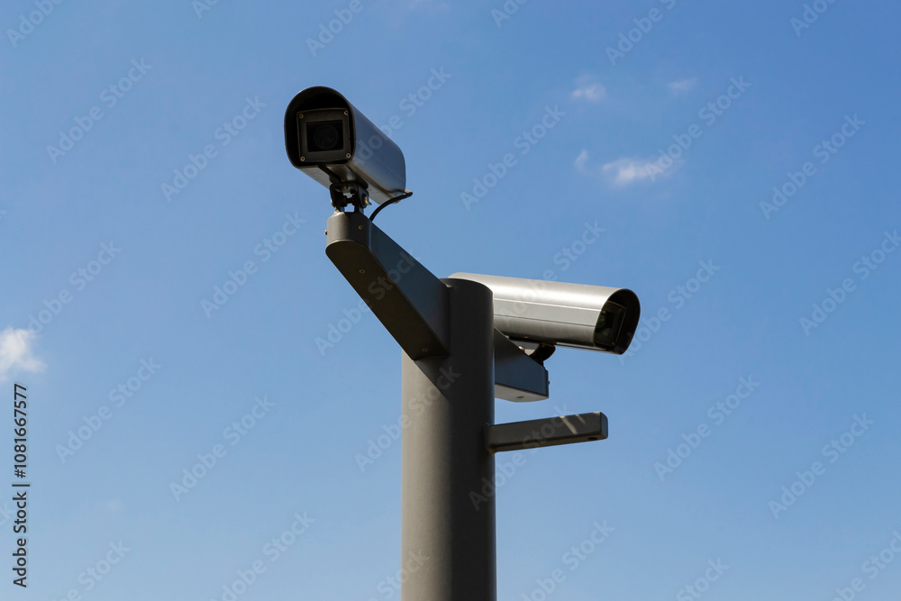 two security cameras mounted on a pole against a clear blue sky. two security cameras mounted on a pole against a clear blue sky.