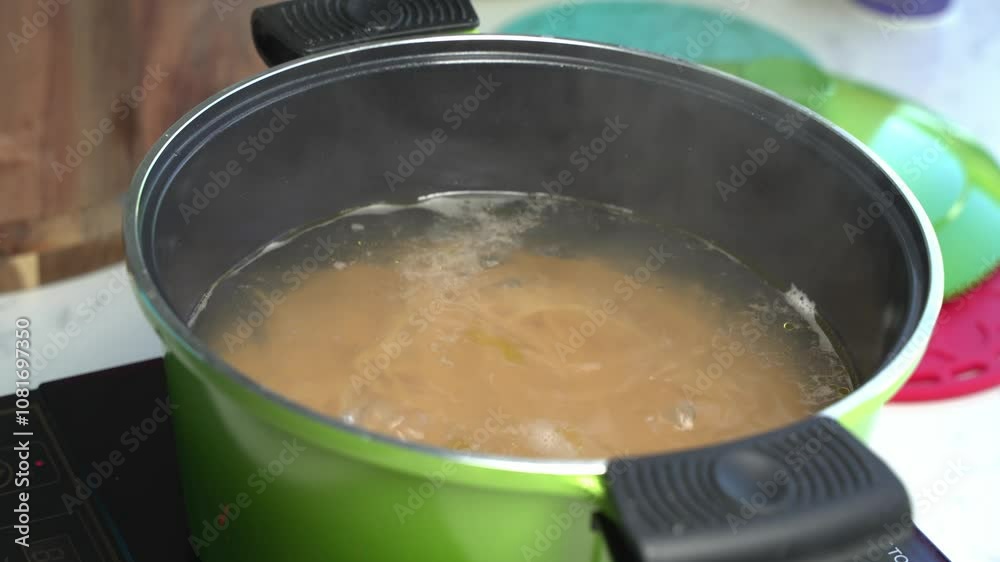 Hand lifting spaghetti from boiling water to check doneness, steam rising from pot Hand lifting spaghetti from boiling water to check doneness, steam rising from pot
