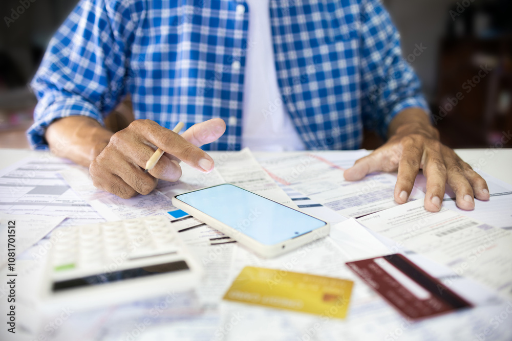 Asian man sitting at desk using mobile phone for online shopping and checking receipt, expenses that must be paid at the end of the month from credit card spending Asian man sitting at desk using mobile phone for online shopping and checking receipt, expenses that must be paid at the end of the month from credit card spending