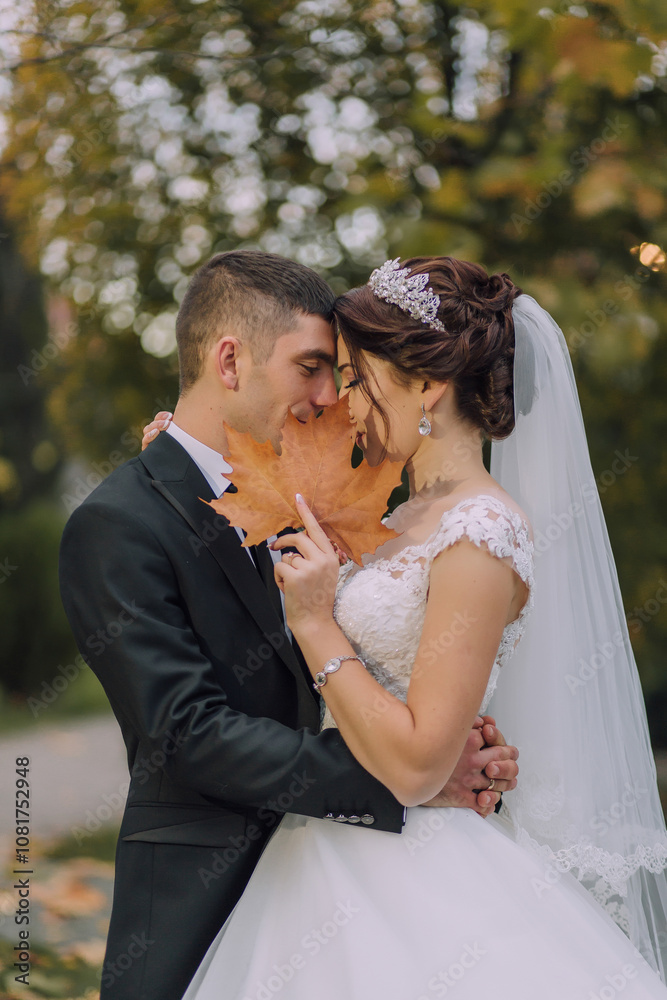 A bride and groom are embracing each other with a leaf in their hands. Scene is romantic and intimate A bride and groom are embracing each other with a leaf in their hands. Scene is romantic and intimate