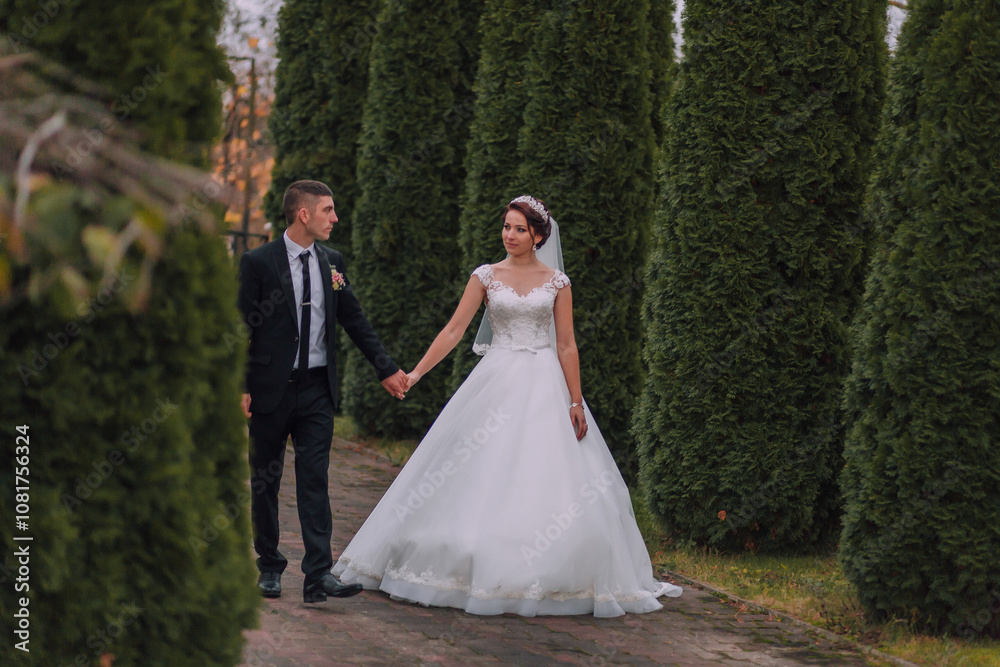 A bride and groom are walking down a path in a forest. The bride is wearing a white dress and the groom is wearing a suit A bride and groom are walking down a path in a forest. The bride is wearing a white dress and the groom is wearing a suit