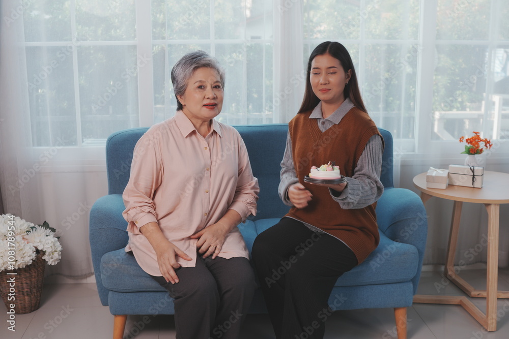 Asian daughter holds birthday cake and delivers it to her mother, making them both happy together.