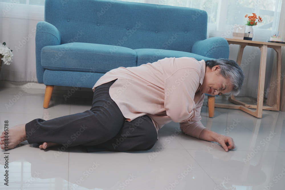 An elderly woman with gray hair falls down on the floor of a room with shoulder pain, suffering from pain in her stomach in the living room at home. An elderly woman with gray hair falls down on the floor of a room with shoulder pain, suffering from pain in her stomach in the living room at home.