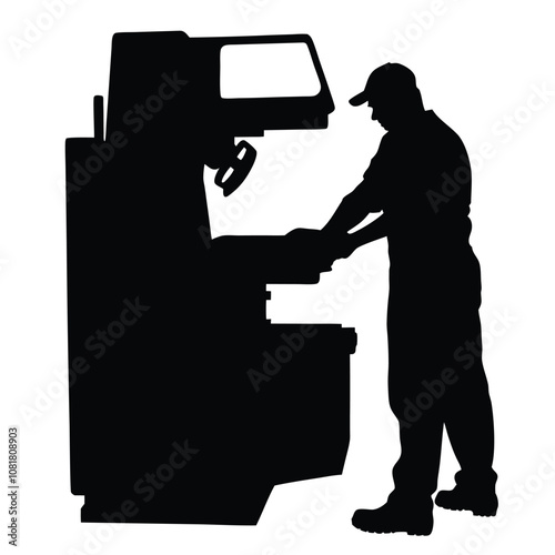 A man is working on a machine. The machine is black and has a large wheel. The man is wearing a hat