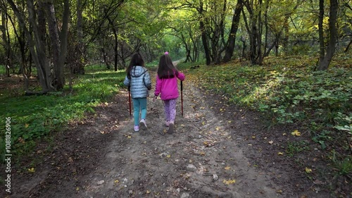 Two little girls walking through the forest. Hiking in mountain with walking sticks. Little discoverers