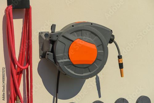 Canvastavla A bright orange retractable hose reel mounted on a garage wall on a sunny aftern