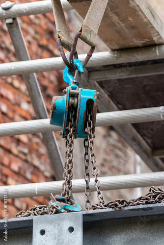 dustrial Chain Hoist with Blue Pulley in Construction Setting: Heavy Duty Equipment Against a Brick Wall Background photo