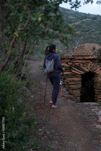 A woman stops to contemplate the natural landscape next to a mountain shelter.