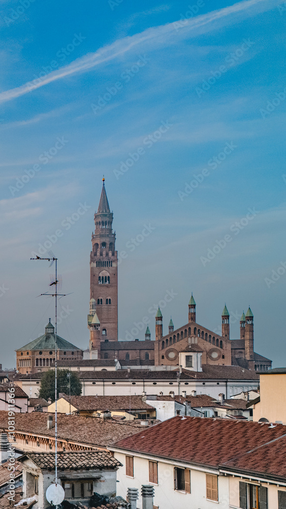 Cremona duomo cathedral towers over the city, blending with rooftops and buildings against blue sky Cremona duomo cathedral towers over the city, blending with rooftops and buildings against blue sky