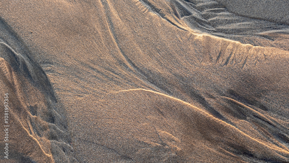 Natural patterns in the beach sand created by wind and waves, highlighted by soft, warm sunlight, form intricate lines and textures in a serene coastal setting. Natural patterns in the beach sand created by wind and waves, highlighted by soft, warm sunlight, form intricate lines and textures in a serene coastal setting.
