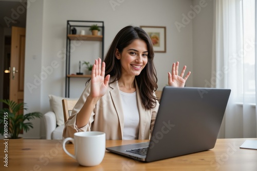 Smiling Businesswoman in Beige Blazer Waving Hello on Laptop Video Call in Cozy Home Office with Coffee Mug photo